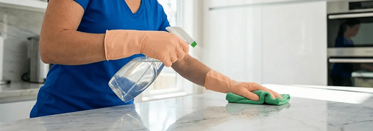 Maid service worker spraying and wiping a kitchen countertop with a microfiber cloth for sanitizing, Columbia, SC.
